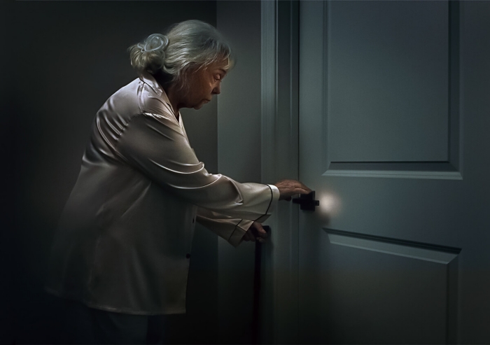 Woman walking through hallway at night with handle on door illuminated